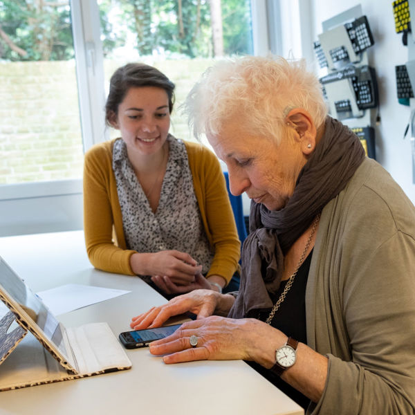 Oudere mevrouw krijgt ondersteuning in het gebruiken van haar telefoon en iPad. Oudere mevrouw krijgt ondersteuning in het gebruiken van haar telefoon en iPad.