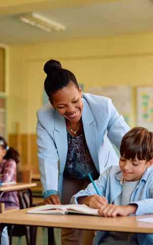 Ambulante onderwijskundige begeleider helpt leerling aan bureau. Ambulante onderwijskundige begeleider helpt leerling aan bureau.