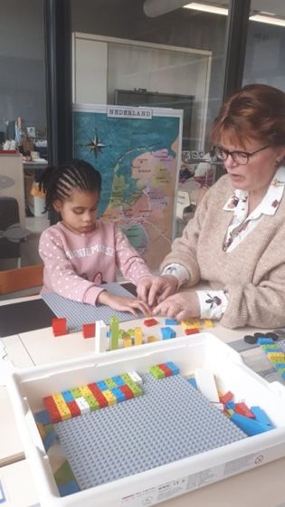 Meisje van kleutergroep Visio Onderwijs Amsterdam voelt aan Lego Braille Bricks met begeleidster