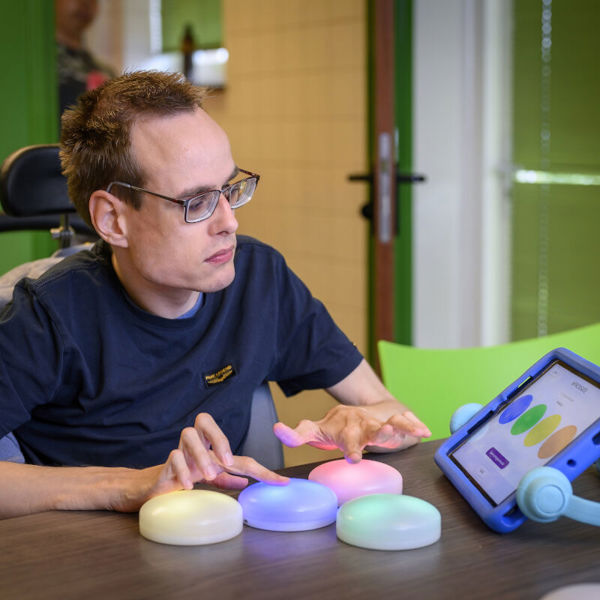 Cliënt met een visuele en verstandelijke beperking doet een tastspel met gekleurde lampen, dat gekoppeld is aan een iPad Cliënt met een visuele en verstandelijke beperking doet een tastspel met gekleurde lampen, dat gekoppeld is aan een iPad