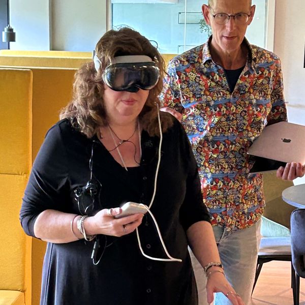 Een cliënt van Visio draagt een VR-bril. Ze is een app aan het testen. Achter haar staat iemand om haar te helpen. Een cliënt van Visio draagt een VR-bril. Ze is een app aan het testen. Achter haar staat iemand om haar te helpen.