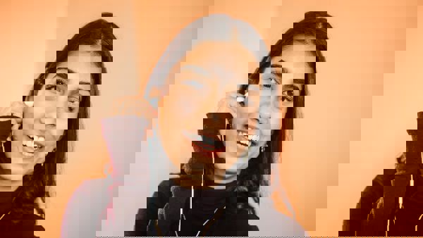 Bodhi zit op haar bed met haar laptop op schoot. Ze doet een oordopje in, en glimlacht naar de camera. Bodhi zit op haar bed met haar laptop op schoot. Ze doet een oordopje in, en glimlacht naar de camera.