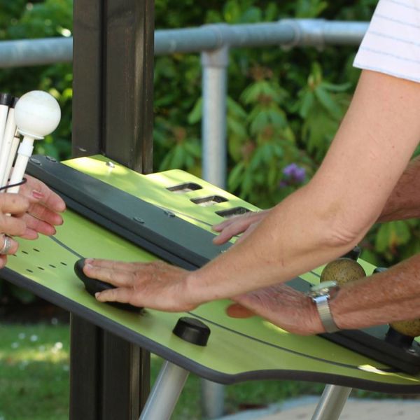Oudere gebruikt een toestel in de beweegtuin van Visio De Vlasborch onder begeleiding van een medewerker Oudere gebruikt een toestel in de beweegtuin van Visio De Vlasborch onder begeleiding van een medewerker