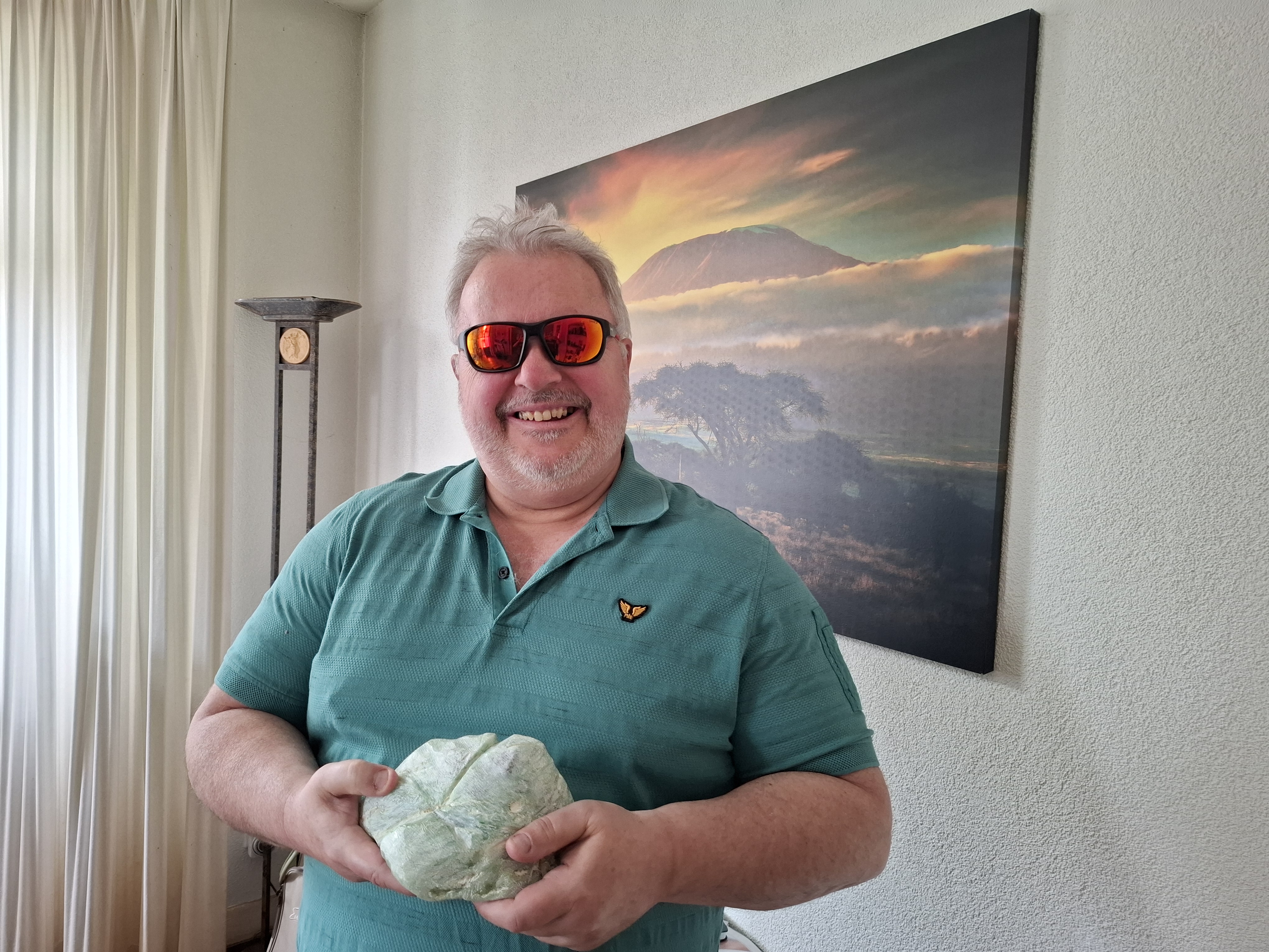 Joska Wolthuis laat zijn speksteen aan de camera zien. Hij draagt een zonnebril en glimlacht naar de camera. 
