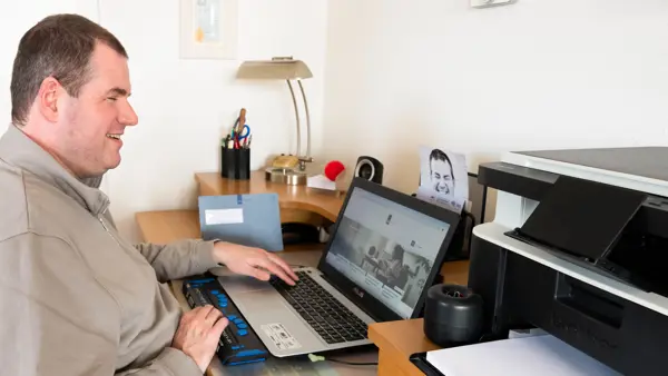 Ralf zit achter zijn laptop aan een bureau. Hij lacht. Ralf zit achter zijn laptop aan een bureau. Hij lacht.