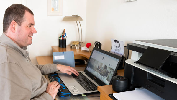 Ralf zit achter zijn laptop aan een bureau. Hij lacht. Ralf zit achter zijn laptop aan een bureau. Hij lacht.