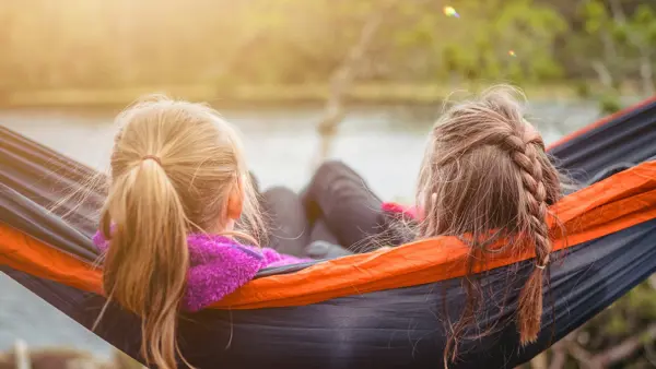 Twee meisjes liggen in een hangmat en kijken uit op een meer en bomen Twee meisjes liggen in een hangmat en kijken uit op een meer en bomen