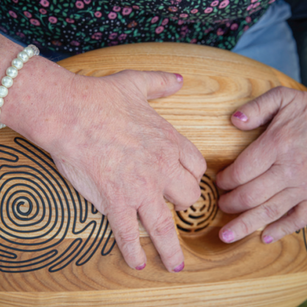 Twee handen houden de CRDL vast. Het is een houten ovaal met gegrafeerde lijnen erop. Twee handen houden de CRDL vast. Het is een houten ovaal met gegrafeerde lijnen erop.