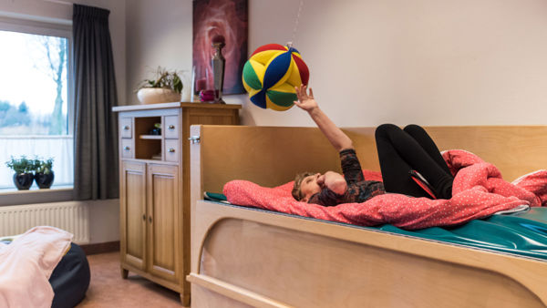 Cliënt speelt met een zachte bal terwijl zij op een bed ligt Cliënt speelt met een zachte bal terwijl zij op een bed ligt