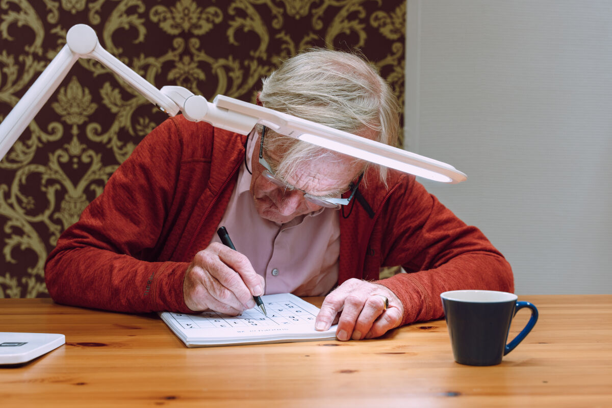 Slechtziende man gebruikt speciale leesbril met leeslamp 