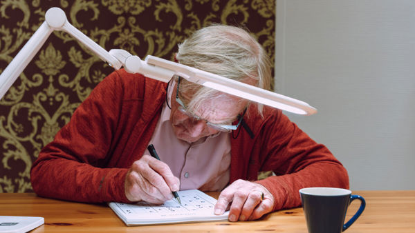 Slechtziende man gebruikt speciale leesbril met leeslamp Slechtziende man gebruikt speciale leesbril met leeslamp