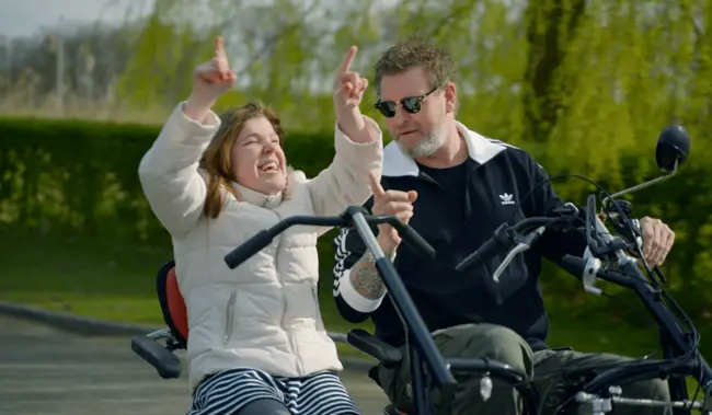 Lachende cliënt met visuele en verstandelijke beperking en begeleider fietsen op een duofiets Lachende cliënt met visuele en verstandelijke beperking en begeleider fietsen op een duofiets