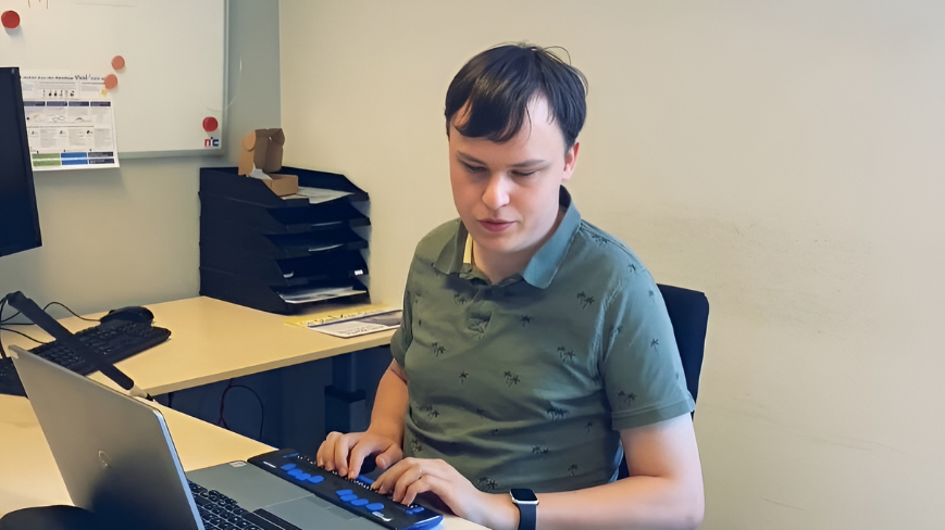 Visio leerling Vince zit achter zijn laptop op school. Hij maakt gebruik van een braille leesregel. 
