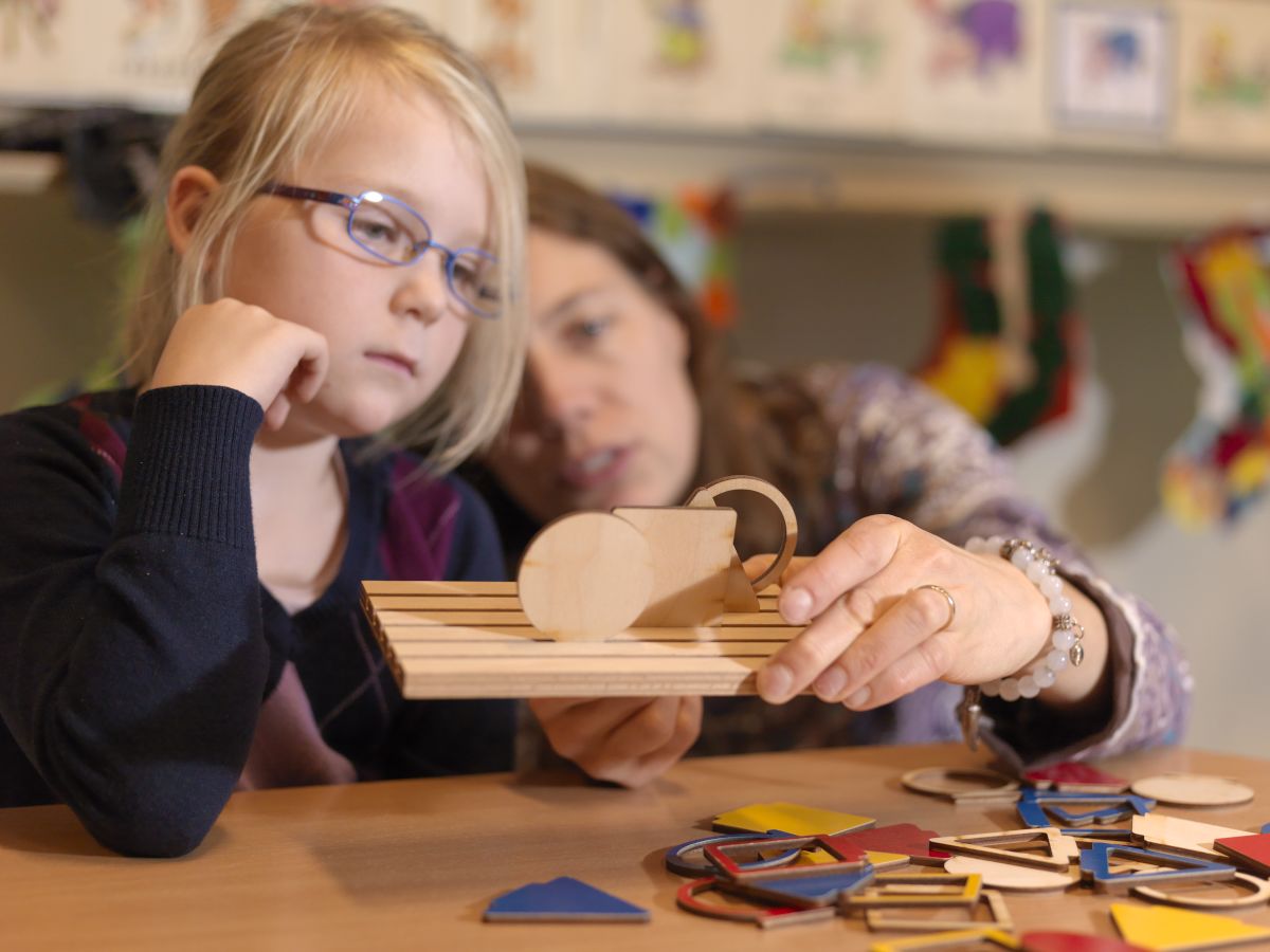 Slechtziend meisje speelt samen met een begeleider met houten speelgoed.