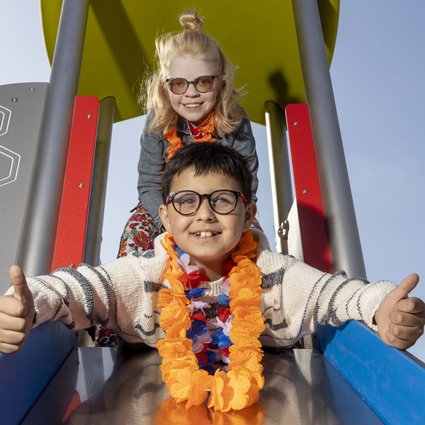Twee kinderen, een jongen en een meisje, gaan samen van de glijbaan af. De jongen steekt zijn duimen omhoog. Twee kinderen, een jongen en een meisje, gaan samen van de glijbaan af. De jongen steekt zijn duimen omhoog.