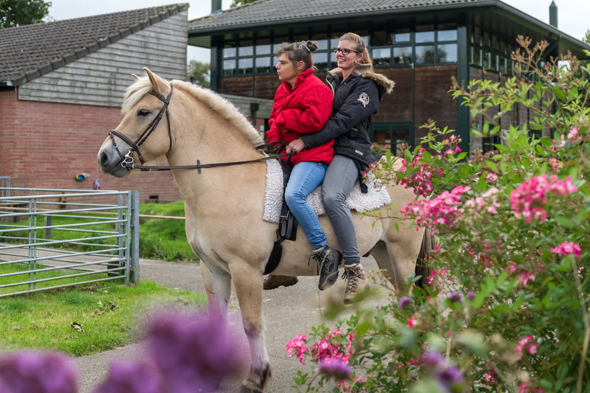 Cliënt en medewerker rijden samen op een paard