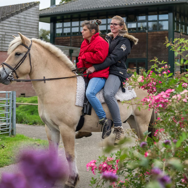 Cliënt en medewerker rijden samen op een paard Cliënt en medewerker rijden samen op een paard