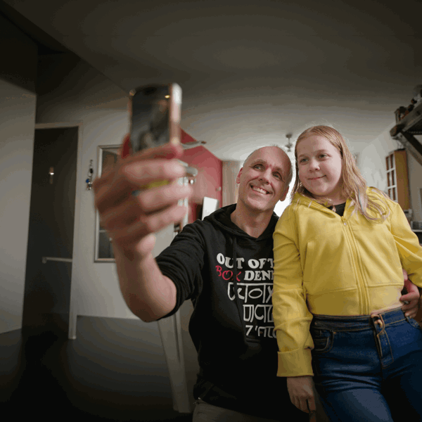 Een slechtziende man van middelbare leeftijd en zijn dochter van ongeveer 13 jaar maken samen een selfie. Ze kijken allebei lachend naar de camera van de telefoon. Een slechtziende man van middelbare leeftijd en zijn dochter van ongeveer 13 jaar maken samen een selfie. Ze kijken allebei lachend naar de camera van de telefoon.