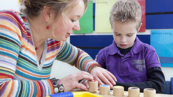 Begeleider helpt leerling met blokken spelen. Begeleider helpt leerling met blokken spelen.