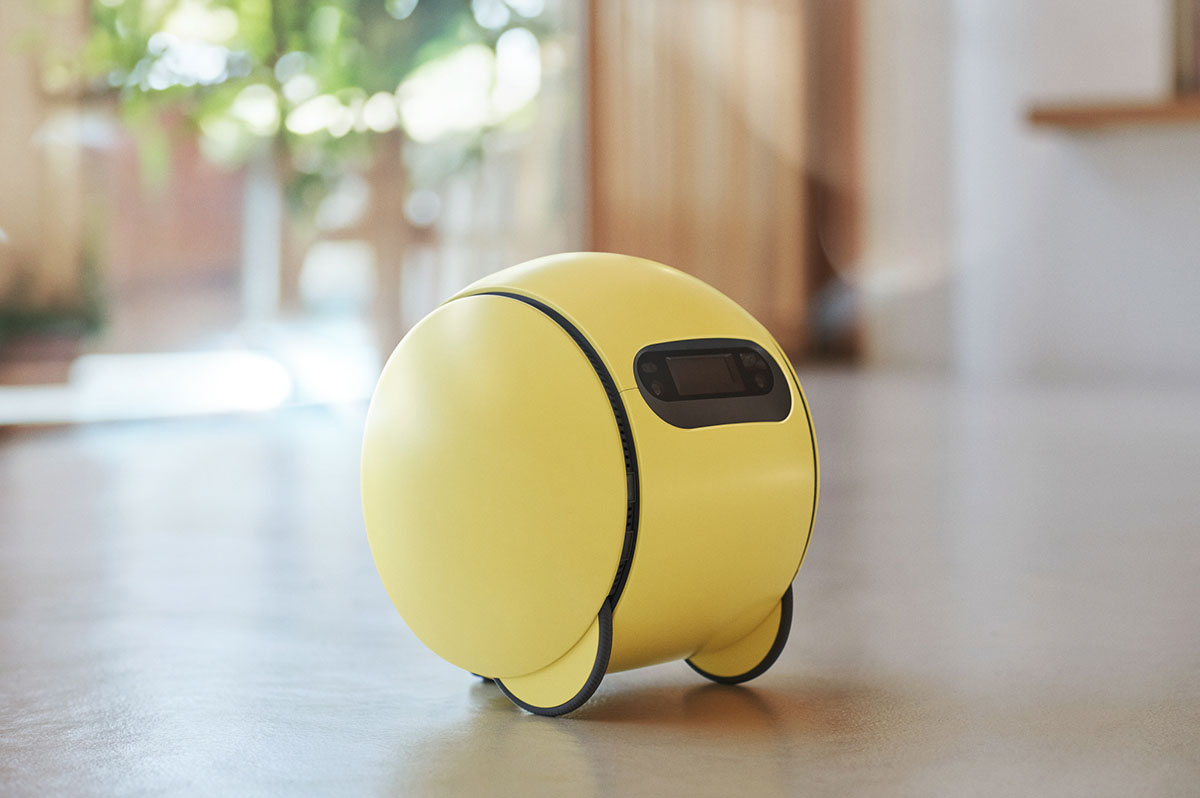Foto (Samsung): Ballie – een kleine, gele bolvormige robot met een zwart schermpje aan de voorkant, staand op een gladde vloer.