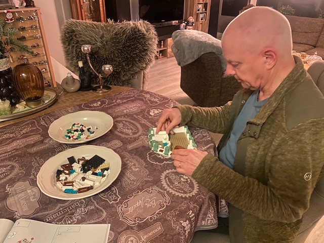 Fred zit aan een ronde tafel. Hij is bezig met een bouwpakket. De onderdelen liggen op twee borden voor hem. 