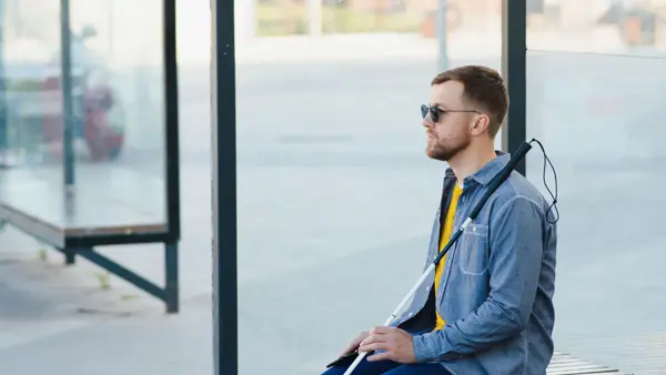 Slechtziende man zit met taststok op de bus te wachten Slechtziende man zit met taststok op de bus te wachten