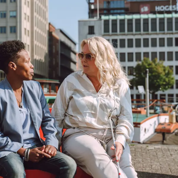 Slechtziende vrouw praat op een bankje met een andere vrouw Slechtziende vrouw praat op een bankje met een andere vrouw