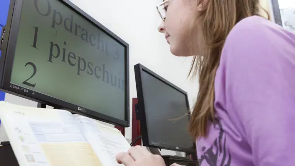 Meisje zit achter een beeldscherm waarop een vergroting te zien is van een schoolopdracht Meisje zit achter een beeldscherm waarop een vergroting te zien is van een schoolopdracht