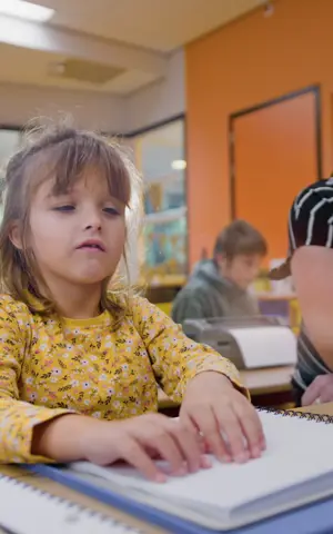 Elena zit in de klas naast de juf. Ze is braille aan het lezen. Elena zit in de klas naast de juf. Ze is braille aan het lezen.