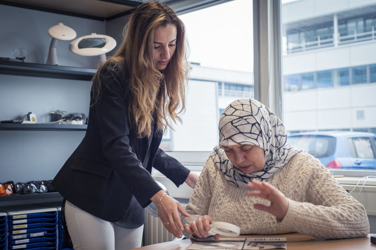 Visio-medewerker begeleidt een allochtone dame die iets leest met een handloep