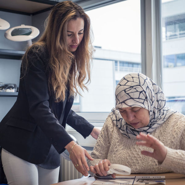 Visio-medewerker begeleidt een allochtone dame die iets leest met een handloep Visio-medewerker begeleidt een allochtone dame die iets leest met een handloep