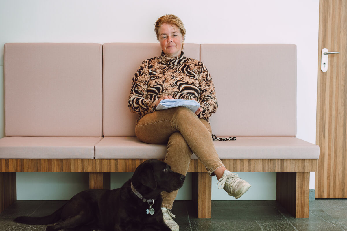 Blinde vrouw zit op bankje met haar geleidehond voor zich