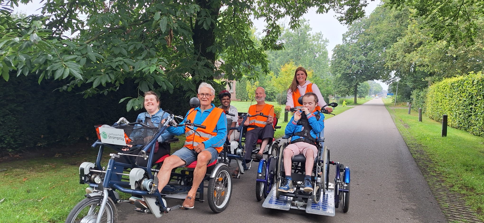 Een aantal vrijwilligers fietsen samen met cliënten in tweepersoonsfietsen. 