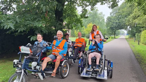 Een aantal vrijwilligers fietsen samen met cliënten in tweepersoonsfietsen. Een aantal vrijwilligers fietsen samen met cliënten in tweepersoonsfietsen.
