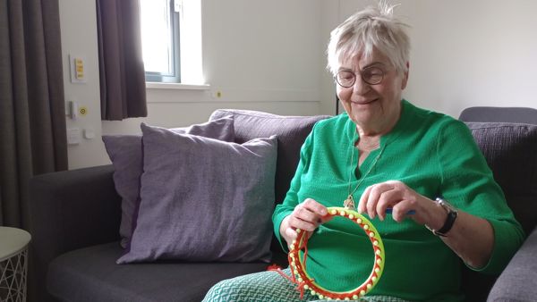 Foto van Sannie die met een breiring creatief aan de slag is, zij draagt een broek met een groen-wit patroon, een groene blouse met mouwen en een bril. Foto van Sannie die met een breiring creatief aan de slag is, zij draagt een broek met een groen-wit patroon, een groene blouse met mouwen en een bril.