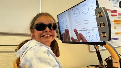 Laura glimlacht naar de camera. Ze draag een zonnebril. Ze zit voor een beeldscherm waarop haar uitvergrootte werkboek te zien is. Laura glimlacht naar de camera. Ze draag een zonnebril. Ze zit voor een beeldscherm waarop haar uitvergrootte werkboek te zien is.