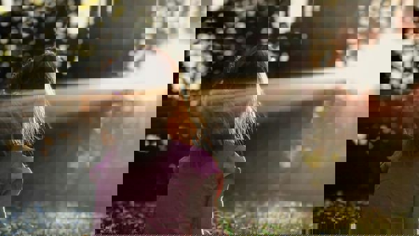 Een meisje zit in het bos op het gras. De zon schijnt door de bomen heen, ze kijkt richting het licht. Een meisje zit in het bos op het gras. De zon schijnt door de bomen heen, ze kijkt richting het licht.