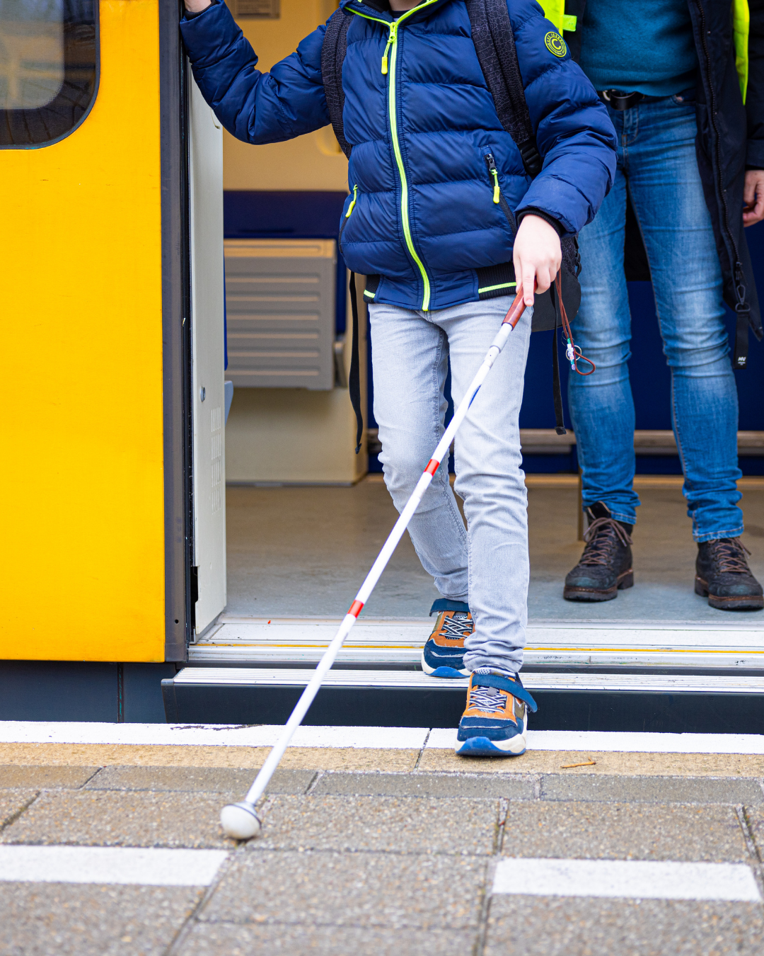 Een jongen stapt uit de trein met zijn taststok. 