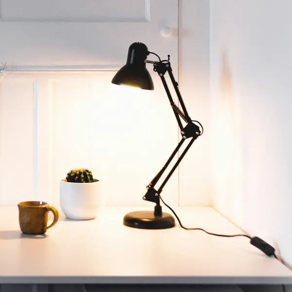 Minimalistische werkplek met een laptop op een wit bureau, naast een mok, een kleine cactus en een brandende bureaulamp. Minimalistische werkplek met een laptop op een wit bureau, naast een mok, een kleine cactus en een brandende bureaulamp.