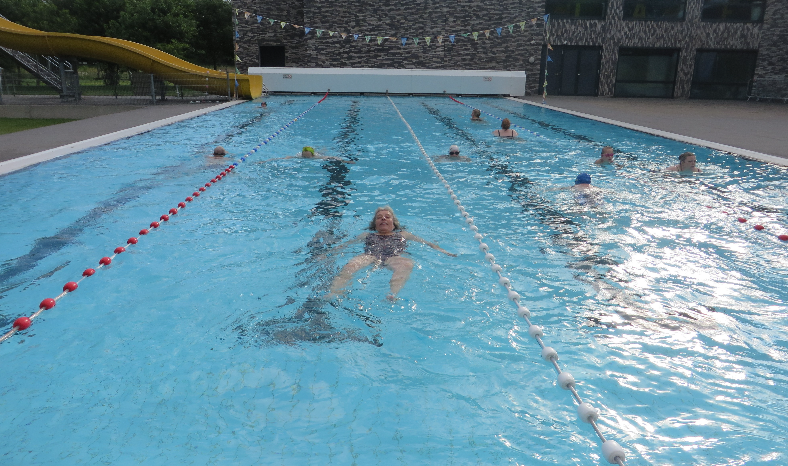 Afbeelding van een zwembad. Meerdere mensen zijn baantjes aan het trekken. 