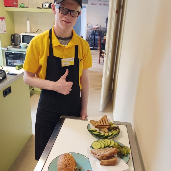 Leerling die bij Visit werkt, poseert lachend bij borden met belegde broodjes en steekt zijn duim op Leerling die bij Visit werkt, poseert lachend bij borden met belegde broodjes en steekt zijn duim op