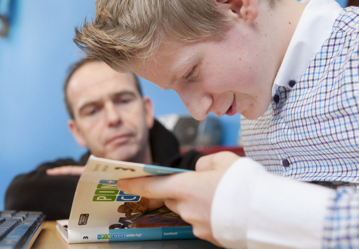 Leerling kijkt in een boek terwijl een docent meekijkt. 