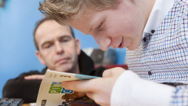 Leerling kijkt in een boek terwijl een docent meekijkt. Leerling kijkt in een boek terwijl een docent meekijkt.