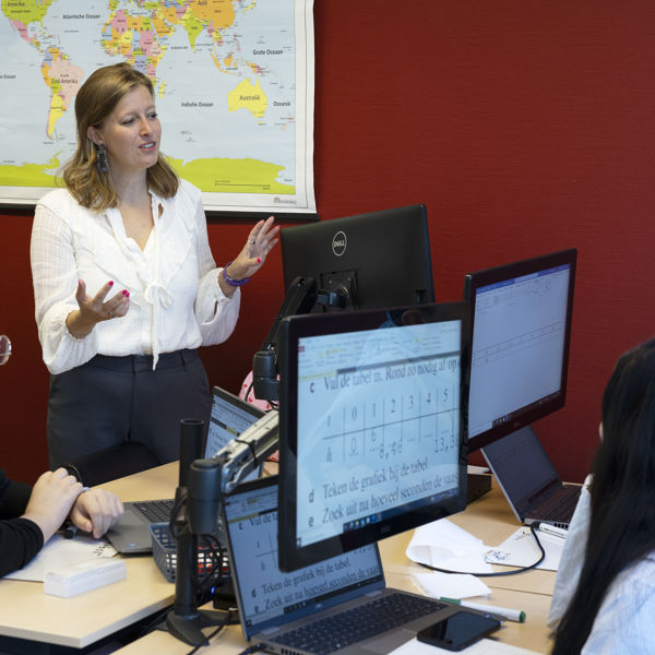 Leerkracht legt uit aan leerlingen die achter een computer aan het werk zijn. Leerkracht legt uit aan leerlingen die achter een computer aan het werk zijn.