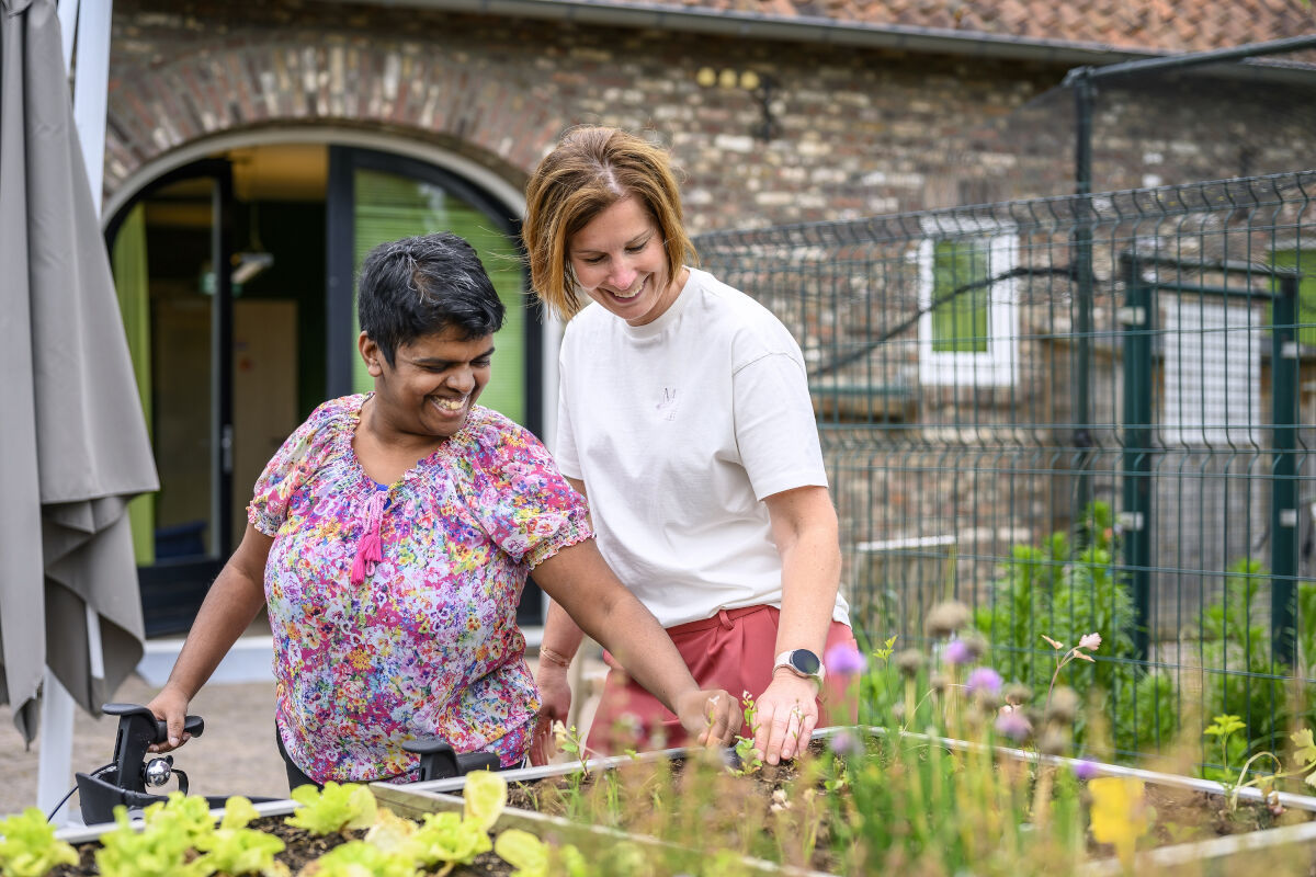 Vrouwelijke cliënt met rollator en een medewerker werken samen bij een verhoogde moestuinbak