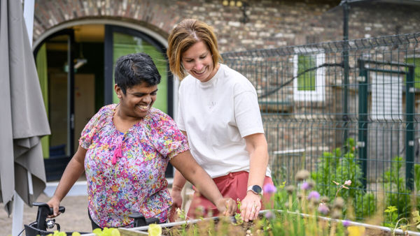 Vrouwelijke cliënt met rollator en een medewerker werken samen bij een verhoogde moestuinbak Vrouwelijke cliënt met rollator en een medewerker werken samen bij een verhoogde moestuinbak