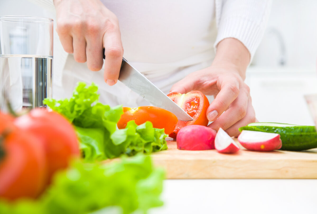 Een close=up van handen die een scherp met vasthouden en groenten snijden. 