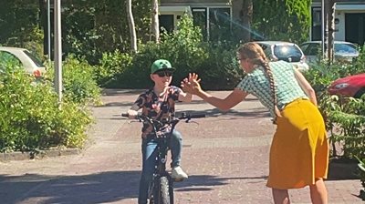 Huang zit op de fiets en geeft zijn ergotherapeut een high-five. 