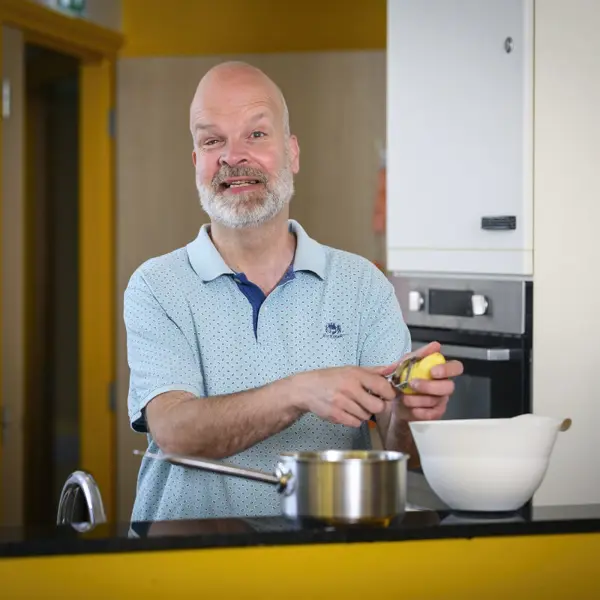 Man schilt aardappels in een keuken op een Visio-locatie en glimlacht daarbij Man schilt aardappels in een keuken op een Visio-locatie en glimlacht daarbij