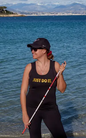 Marie-Elise poseert met haar taststok in een sportieve outfit met de tekst "Just do it" voor een meer met bergen op de achtergrond Marie-Elise poseert met haar taststok in een sportieve outfit met de tekst "Just do it" voor een meer met bergen op de achtergrond